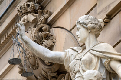 A statue of the goddess Justitia holds a pan of scales in front of the building of the district and regional court.