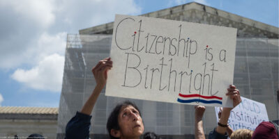 A demonstrator looks up at her sign (which reads "Citizenship is a Birthright") during a rally outside the Supreme court building demanding the court uphold the 14th Amendment to the U.S. Constitution.