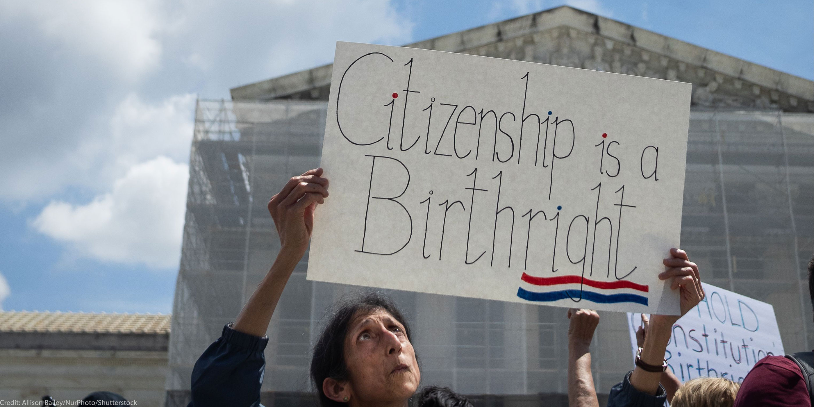 A demonstrator looks up at her sign (which reads "Citizenship is a Birthright") during a rally outside the Supreme court building demanding the court uphold the 14th Amendment to the U.S. Constitution.