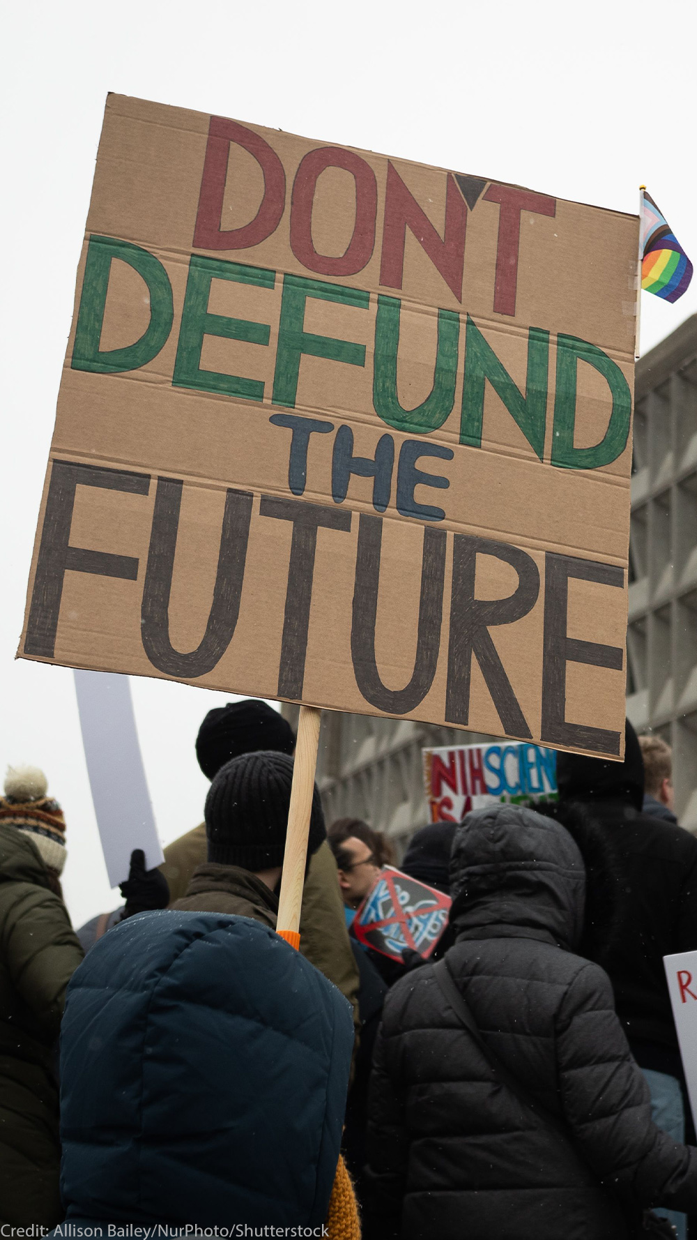 People attend a rally against the Trump administration's 90-day funding freeze and job cuts at health agencies in Washington, DC, hold up a large sign written in red, green and black on cardboard that reads " DON'T DEFUND THE FUTURE."