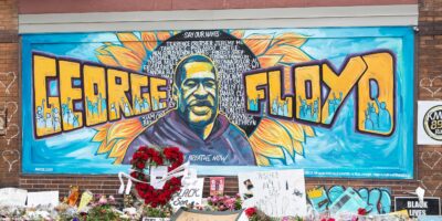 A mural with the image of George Floyd ihas flowers and signs protesting his murder lay beneath it five years later.