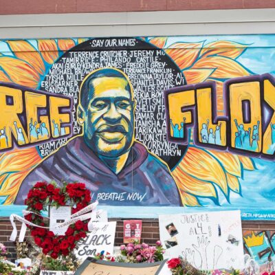 A mural with the image of George Floyd ihas flowers and signs protesting his murder lay beneath it five years later.