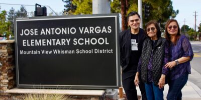 A smiling Jose Antonio Vargas and two equally joyful female family members stand to the right of a large sign that reads "JOSE ANTONIO VARGAS