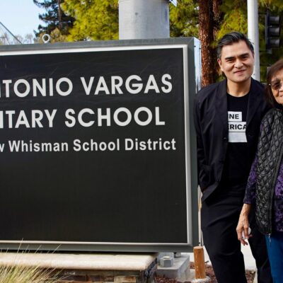 A smiling Jose Antonio Vargas and two equally joyful female family members stand to the right of a large sign that reads "JOSE ANTONIO VARGAS