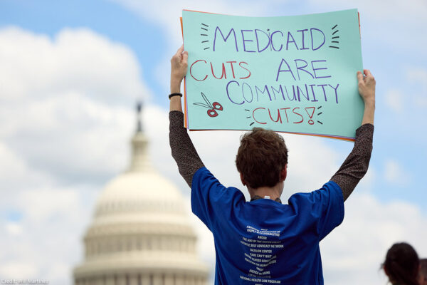 An individual at a 24-hour Vigil and Rally to Protect Medicaid on Capitol Hill, outside of the U.S. Capitol Building, holding a sign that says "Medicaid Cuts Are Community Cuts."
