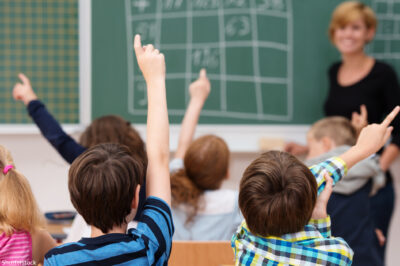 Middle school students raising hands to answer teacher.