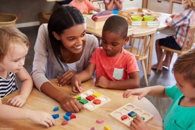 Teacher and pre-K students using wooden shapes.