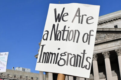 Two signs are held up during the May Day March In Manhattan, New York on May 1, 2025. The largest of the signs is in the foreground and reads"We Are a Nation of Immigrants," while the smaller in the background reads, " WE ARE ALL (EXCEPT NATIVE AMERICANS) IMMIGRANTS! PUT I.C.E. ON ICE NOW".